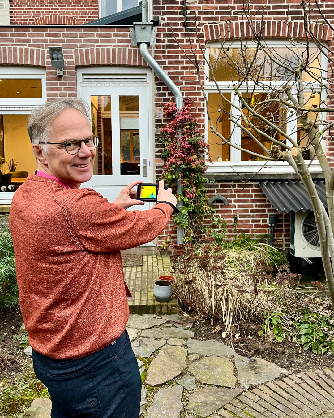 Man die naar de camera kijkt en een warmtescan maakt van zijn huis