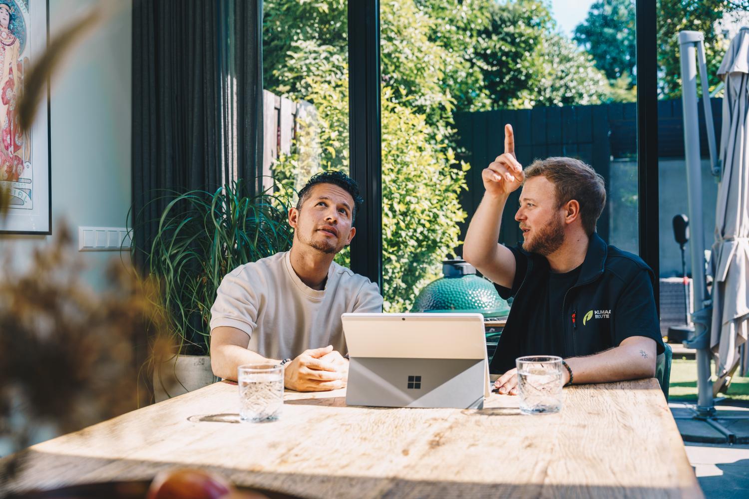 Twee mannen aan tafel die naar iets kijken en wijzen